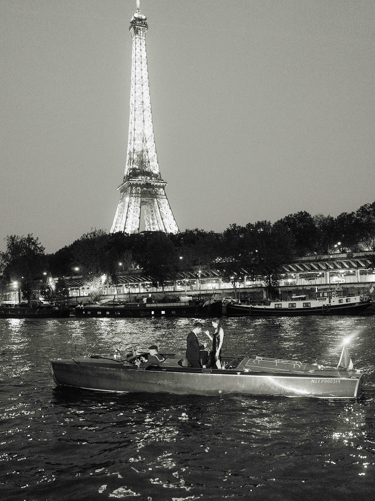 Black and white view of an engaged couple on a boat beneath the Eiffel Tower